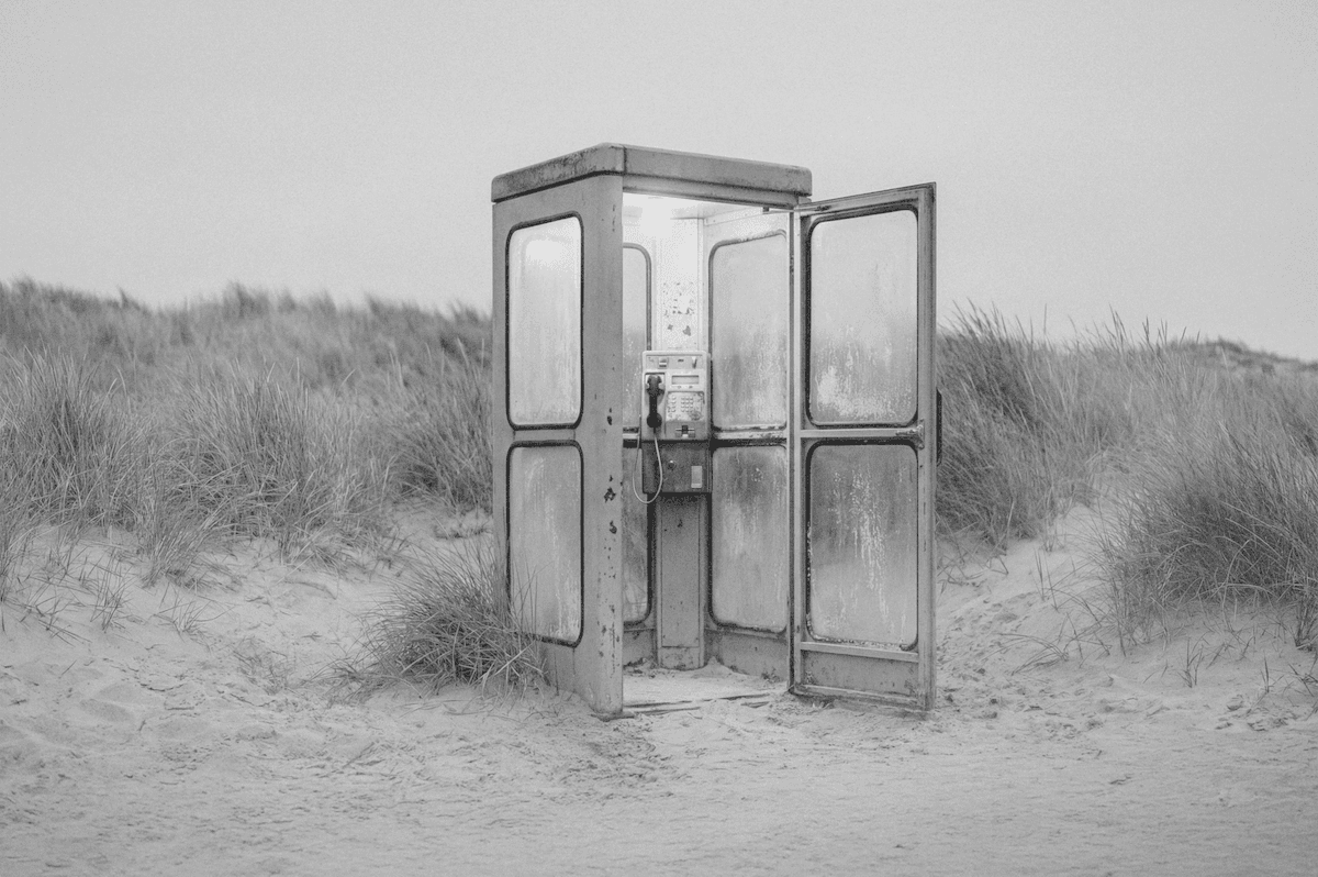 Eine Telefonzelle steht im Sand am Strand vor einer Düne